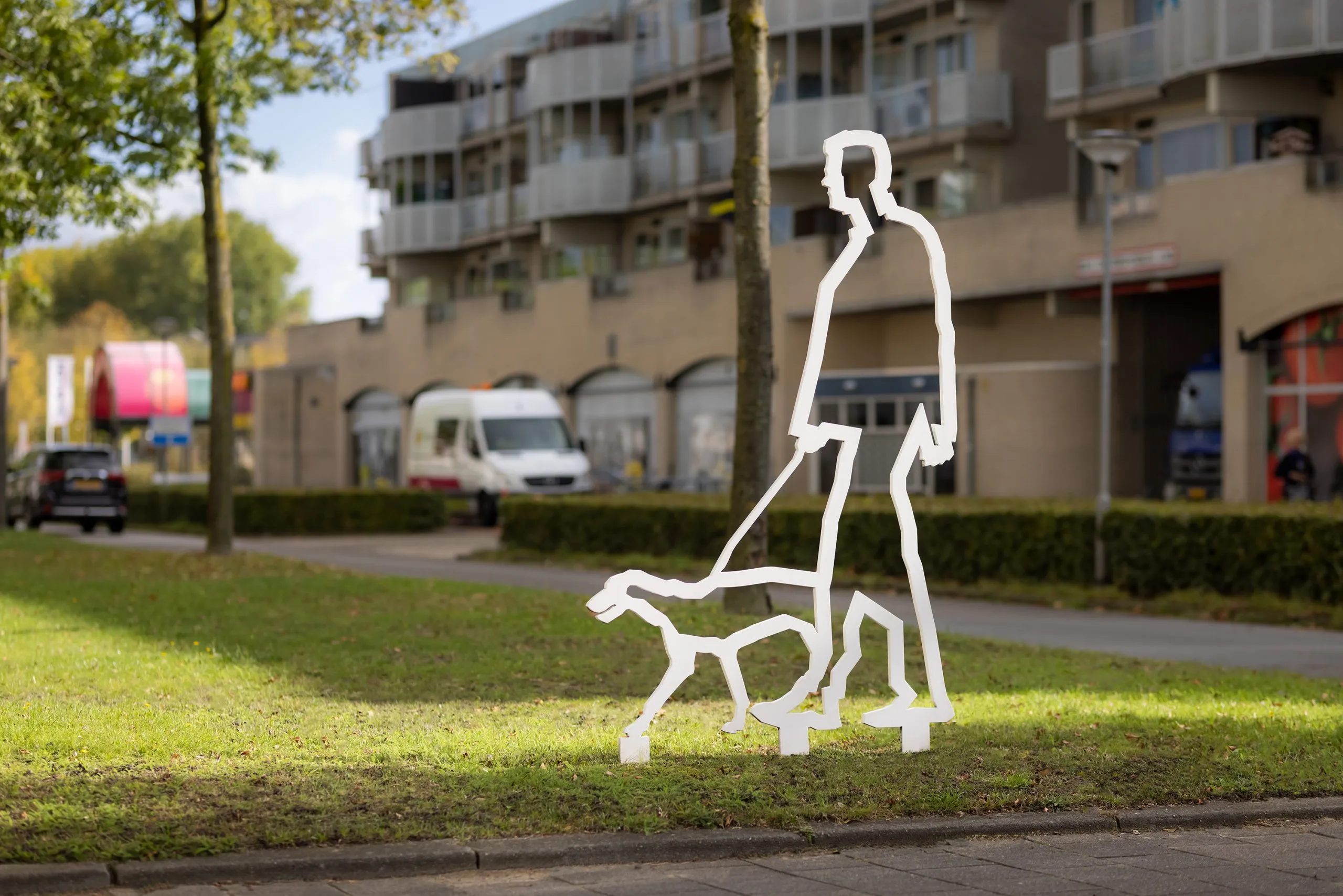 Wit stalen figuur van iemand die een hond uitlaat