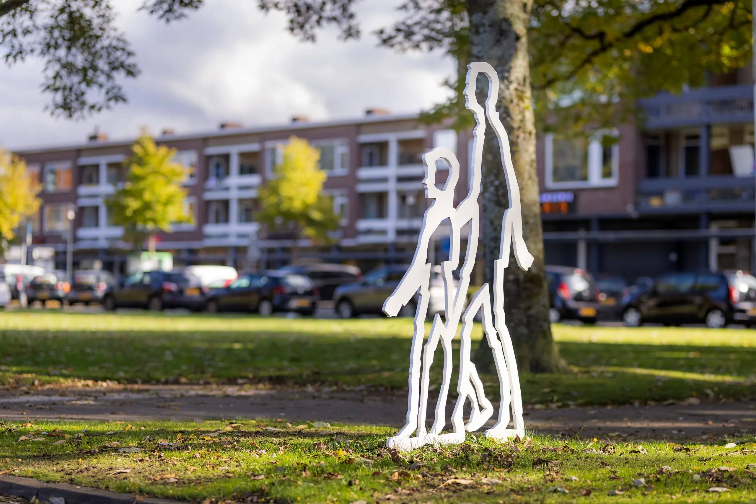 Twee witte stalen wandelfiguren naast elkaar in de berm langs een straat in Breda