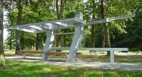 Stalen schuilplek met een luifel en een houten bank aan de rand van een bos