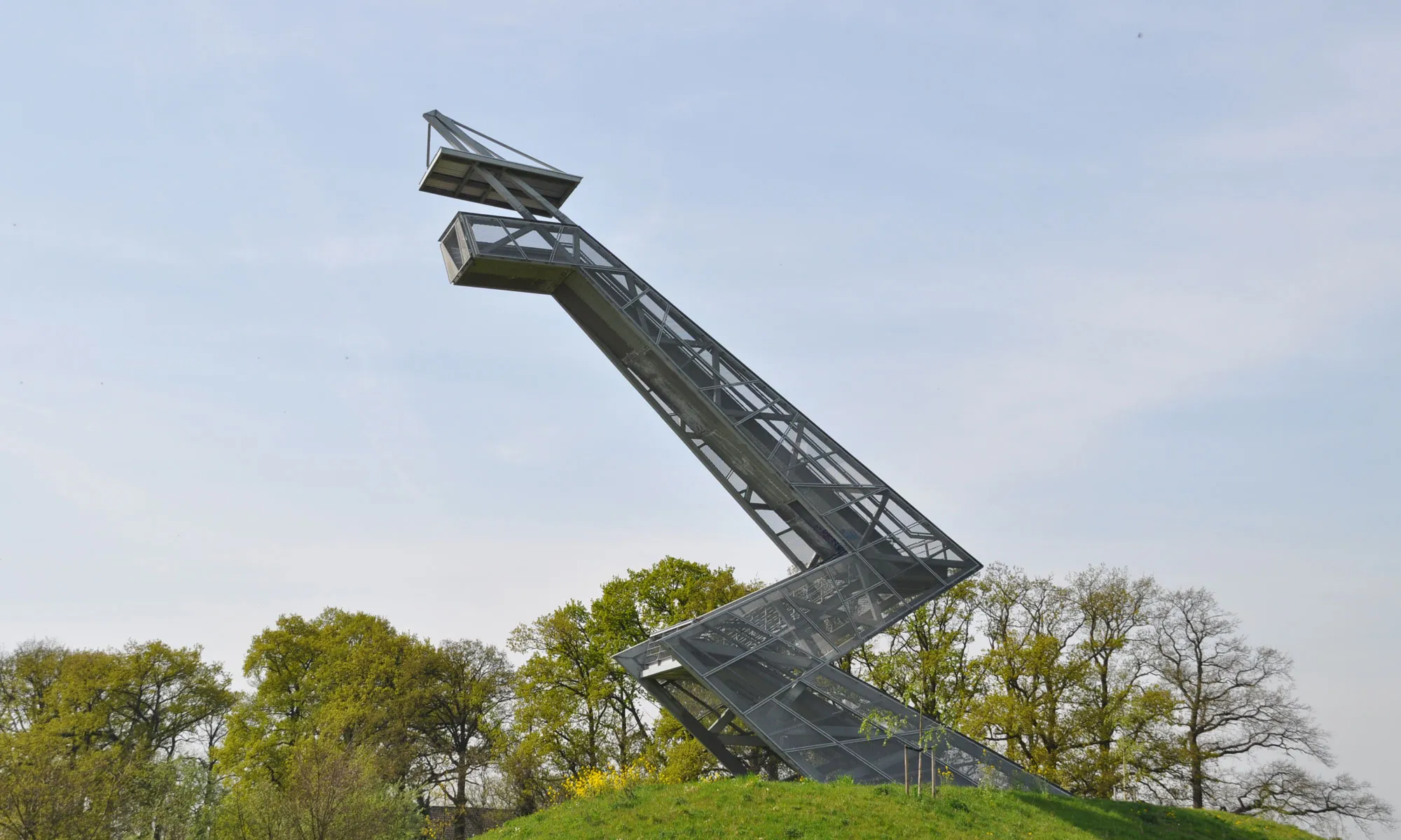 Stalen uitkijktoren met een geknikte vorm op een grasheuvel langs de A16